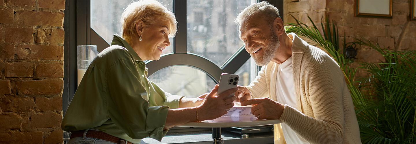 A couple sitting at a table, the woman is showing the man her phone